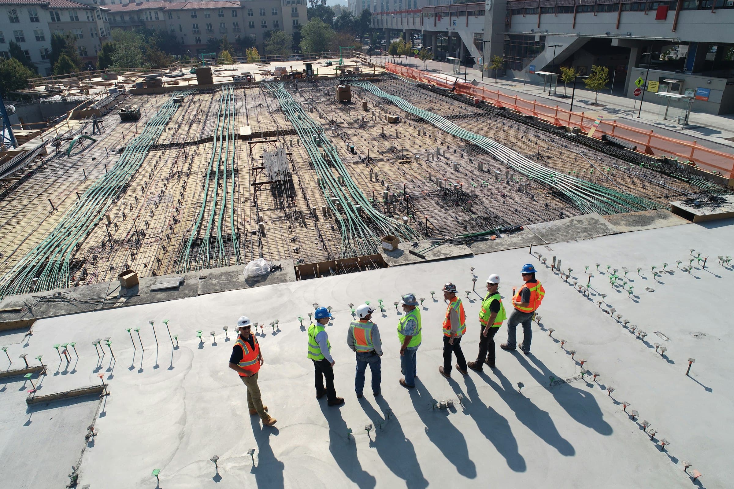 Construction crew in high-visibility vests standing on a concrete slab, casting long shadows across the site